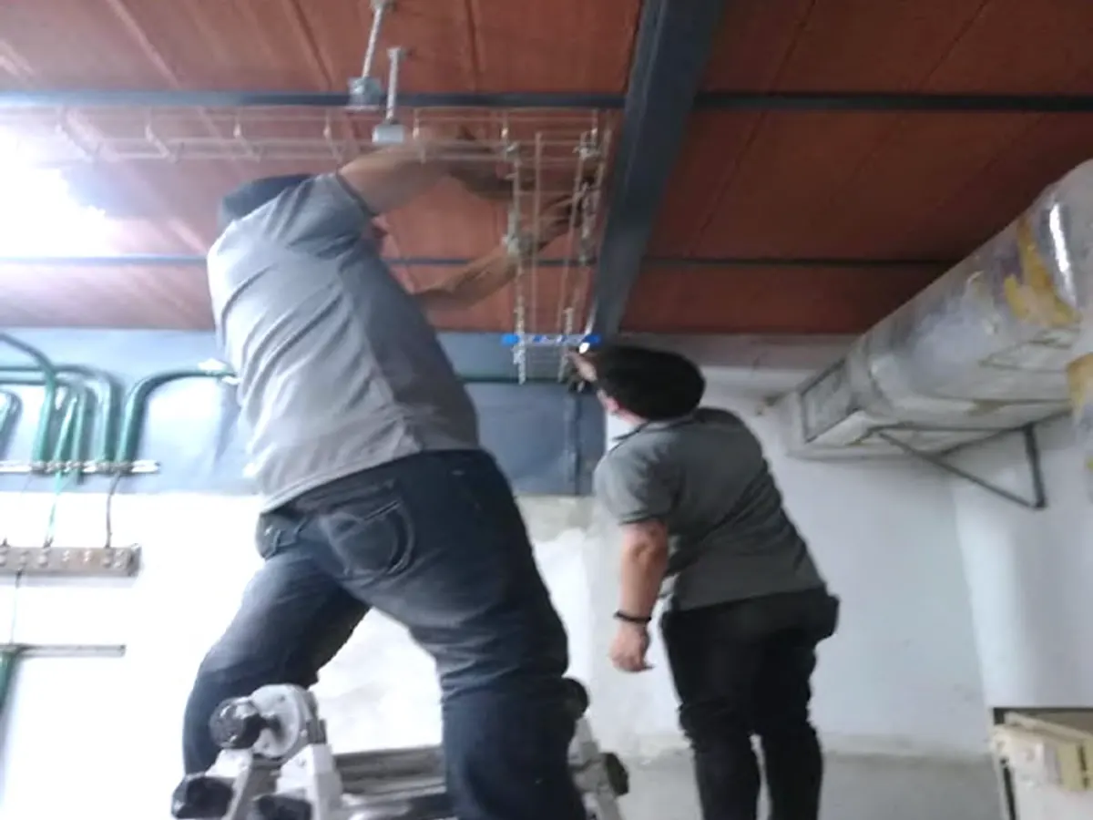Dos técnicos de Favinca instalando bandeja portacables bajo techo