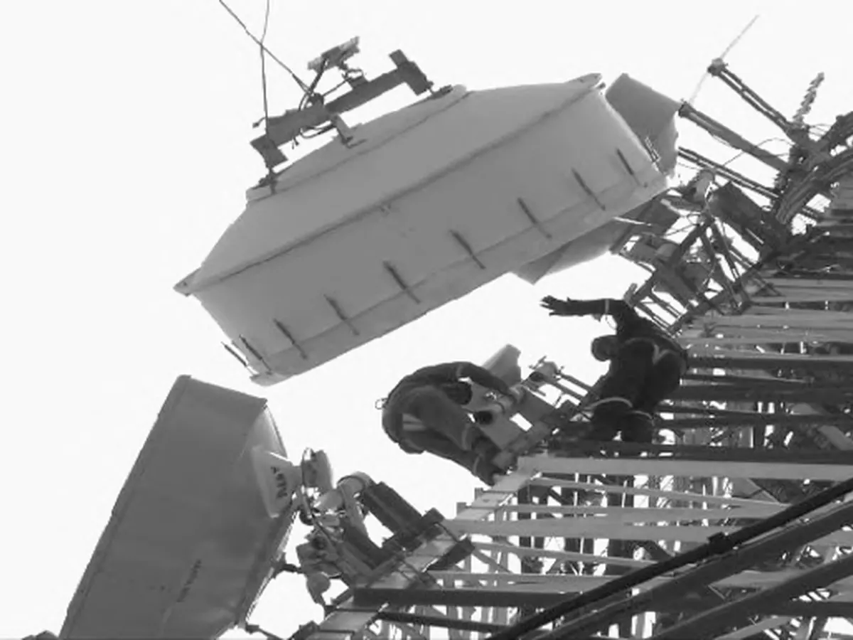 Técnicos izando una antena parabólica en una torre