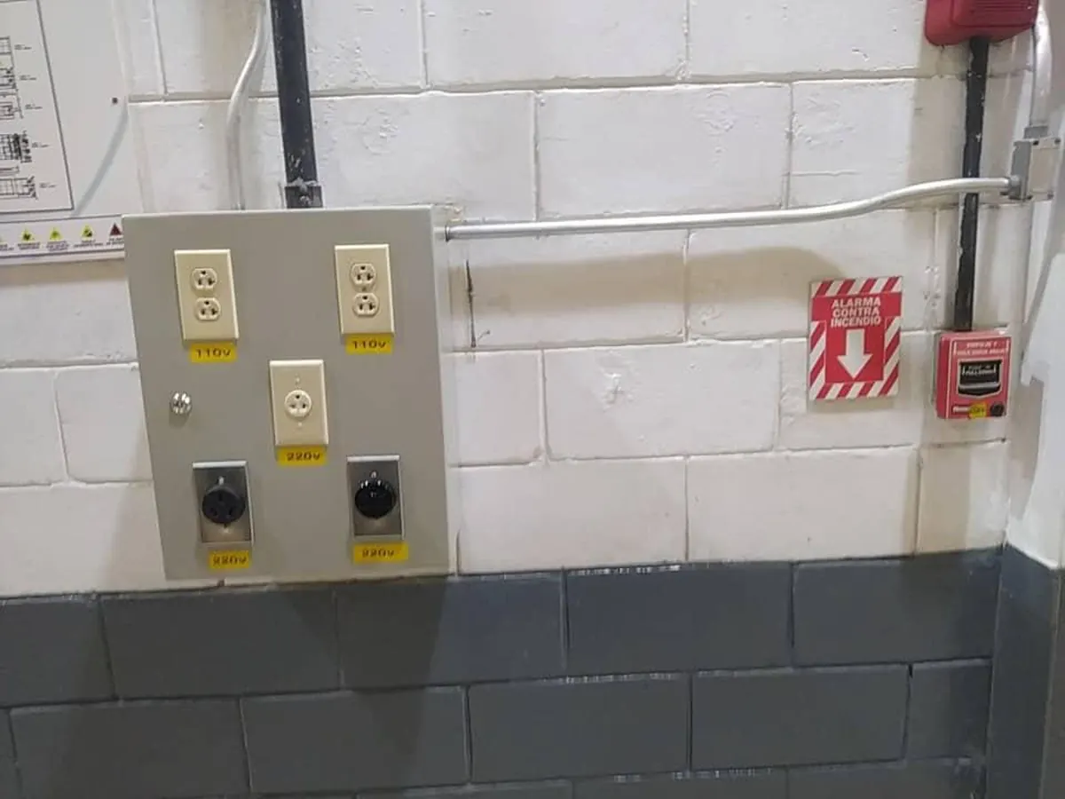 Caja de tomacorrientes de 110 V y 220 V junto a un aviso de alarma contra incendio y una estación manual