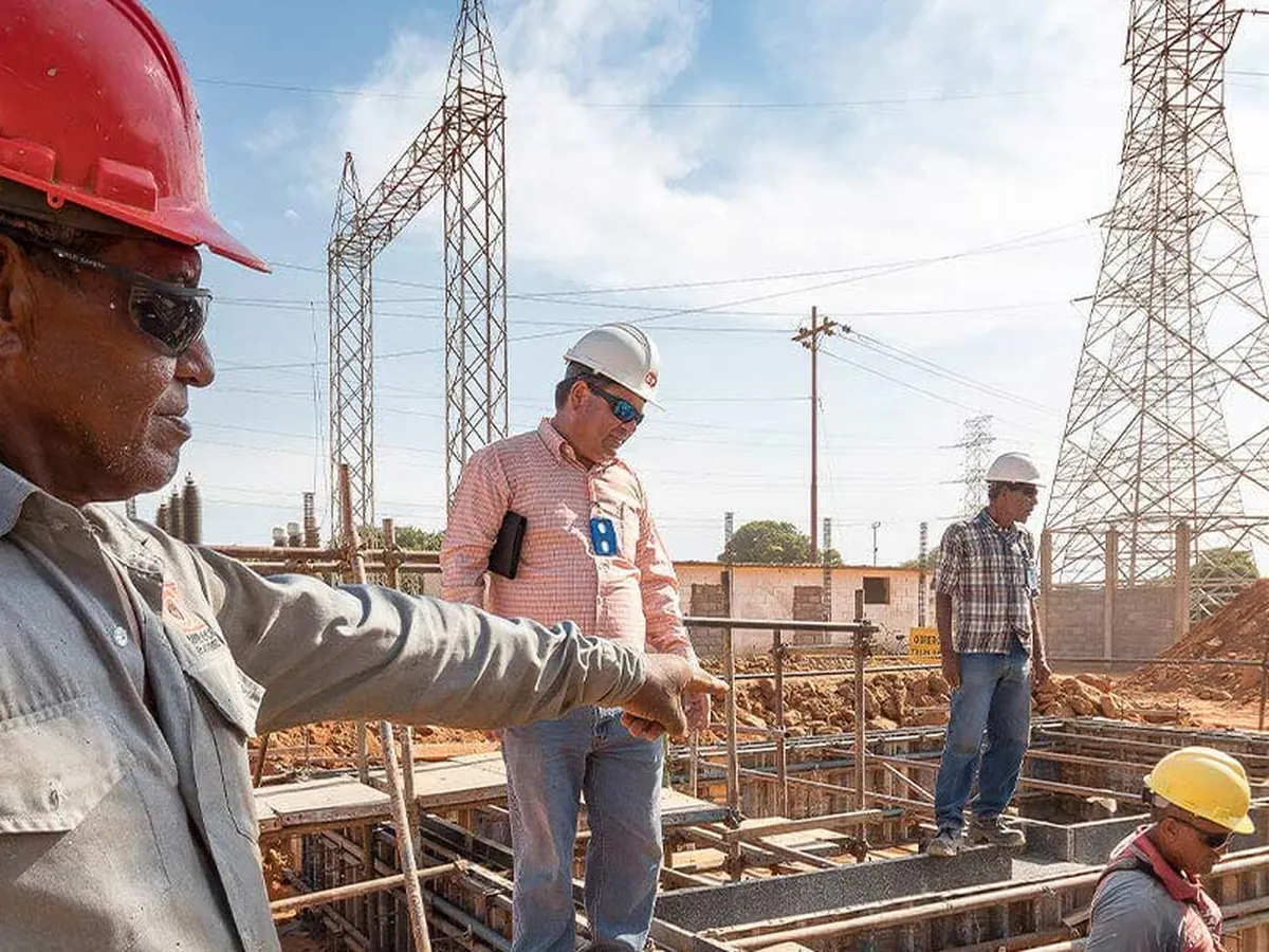 Cuadrilla con cascos en la obra civil de una subestación, con torres de alta tensión al fondo